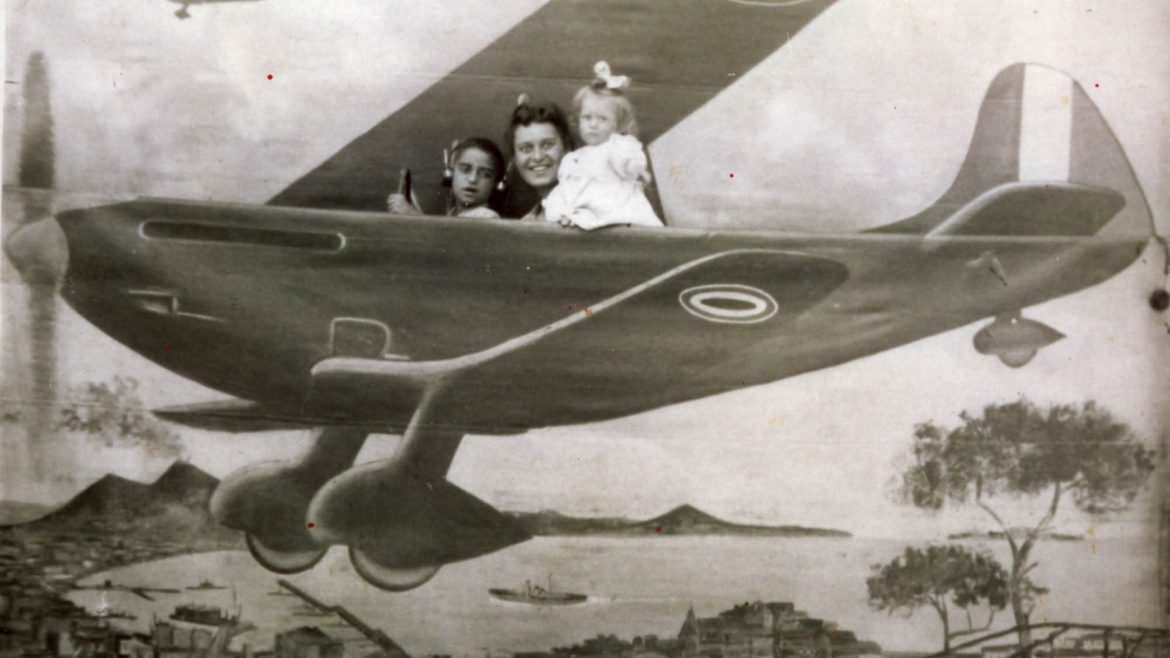 Donna e due bambini sul set di un fotografo ambulante, su fondale dipinto con aeroplano. Tolfa, Rm. © Fondo Adriani