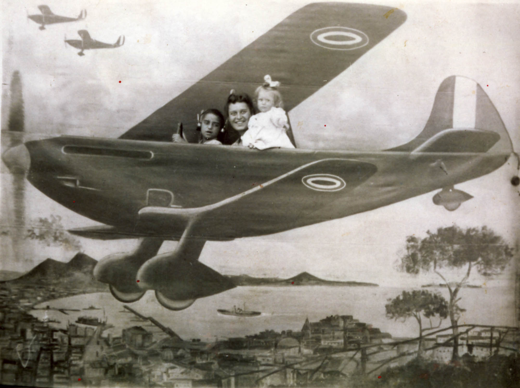 Donna e due bambini sul set di un fotografo ambulante, su fondale dipinto con aeroplano. Tolfa, Rm. © Fondo Adriani